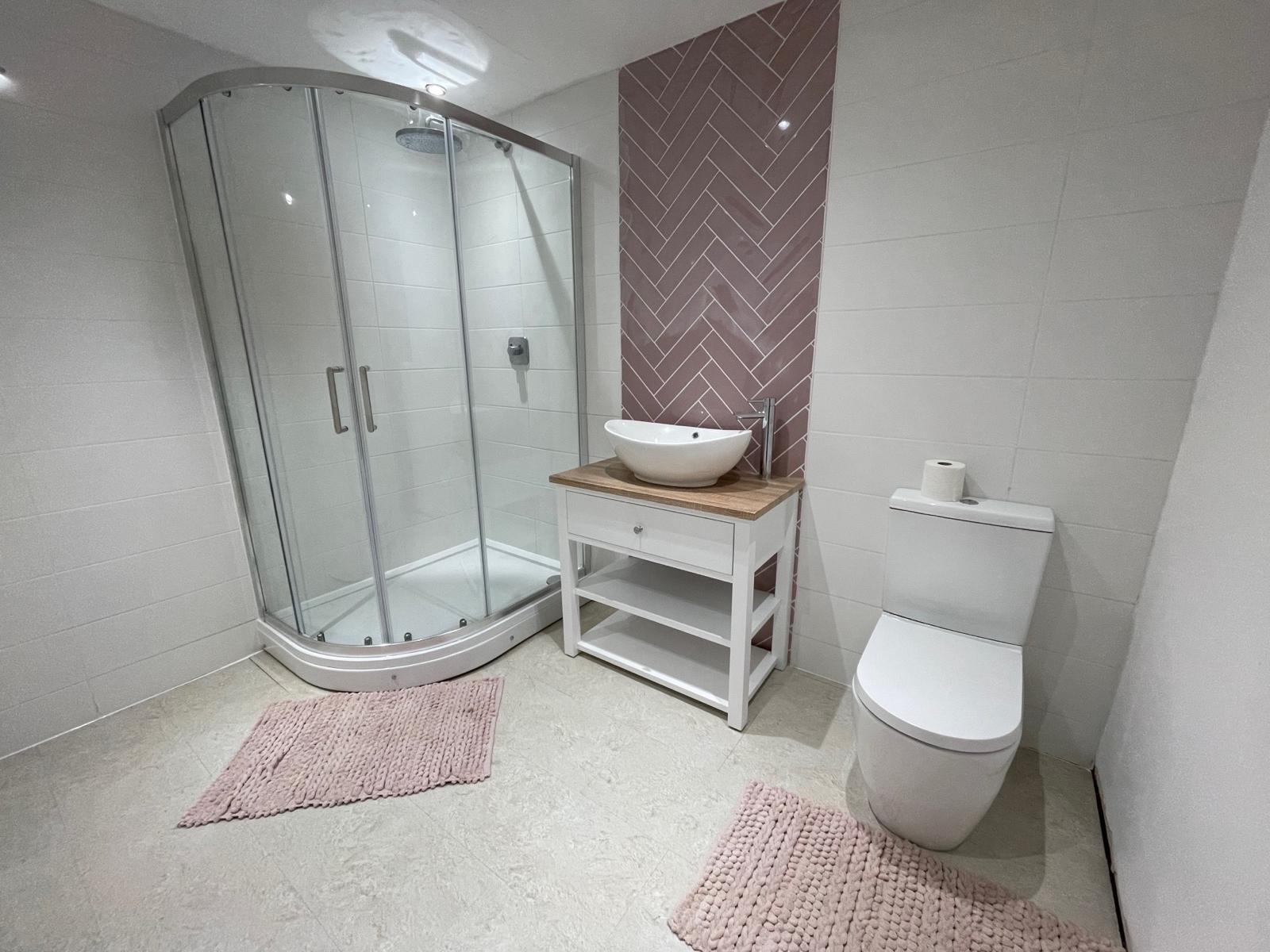 Ensuite with a pink herringbone tile wall, vessel basin and quadrant shower